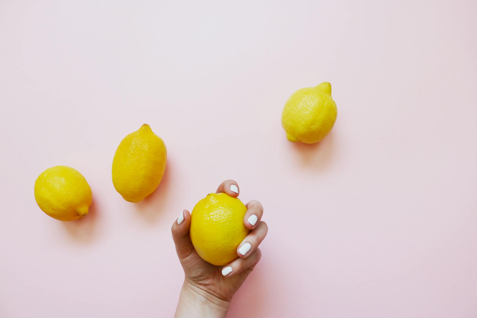 A hand holding a fresh lemon on a soft pink background, symbolizing new beginnings and comfort with intimacy.