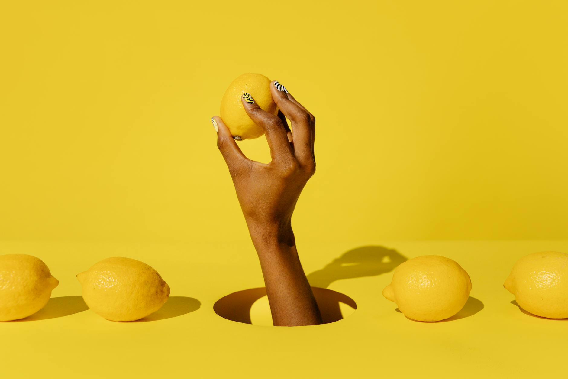 A hand holding a fresh lemon against a vibrant yellow background, symbolizing citrusy intensity and pleasure