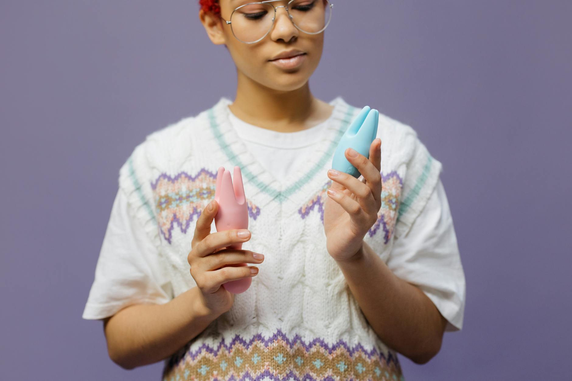 Woman holding blue and pink clitoral vibrators with focused expression