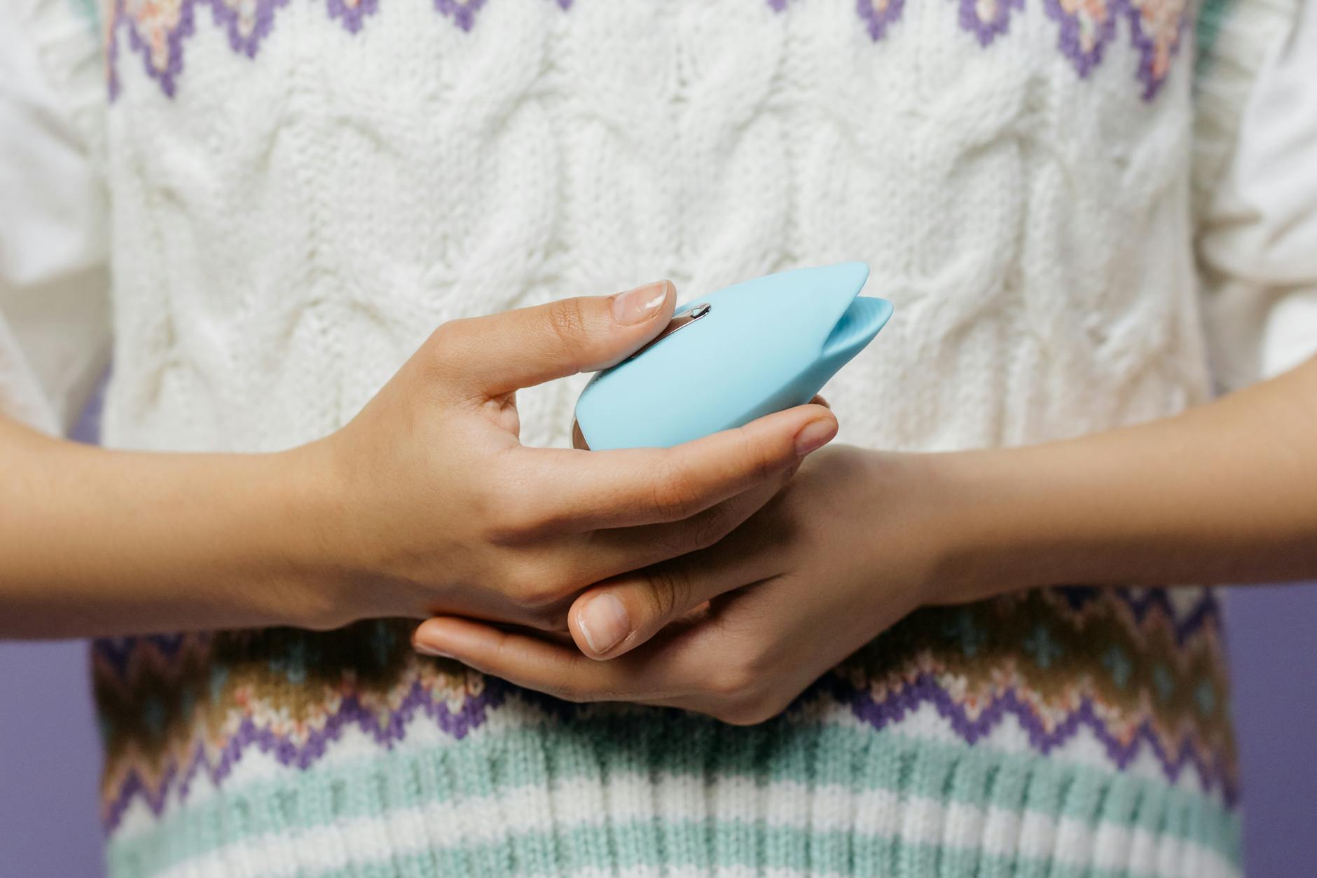 Intimate close-up of hands holding a sleek blue vibrator against a purple background.